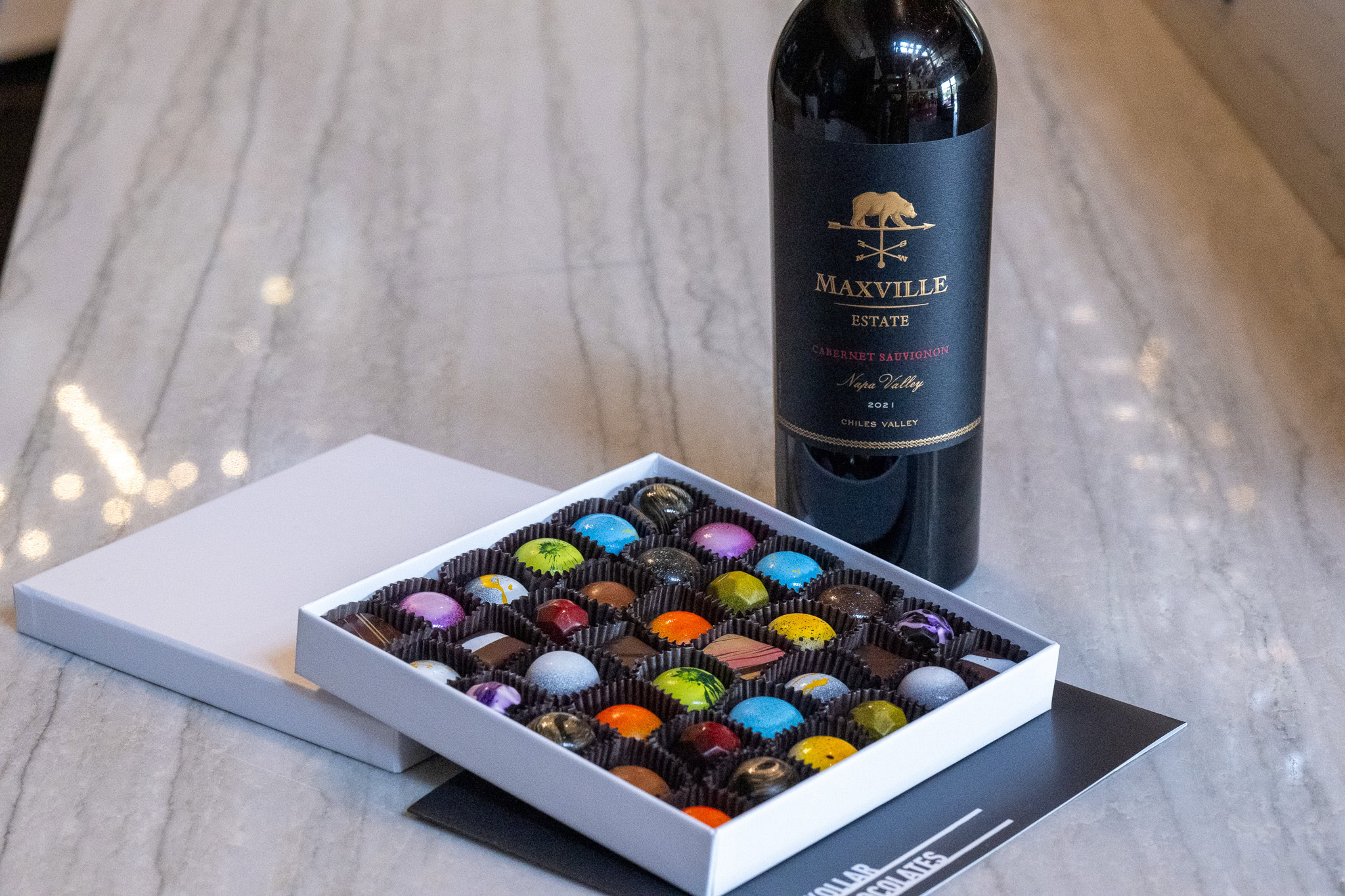 Maxville Winery wine bottle and assorted chocolates on a marble surface.