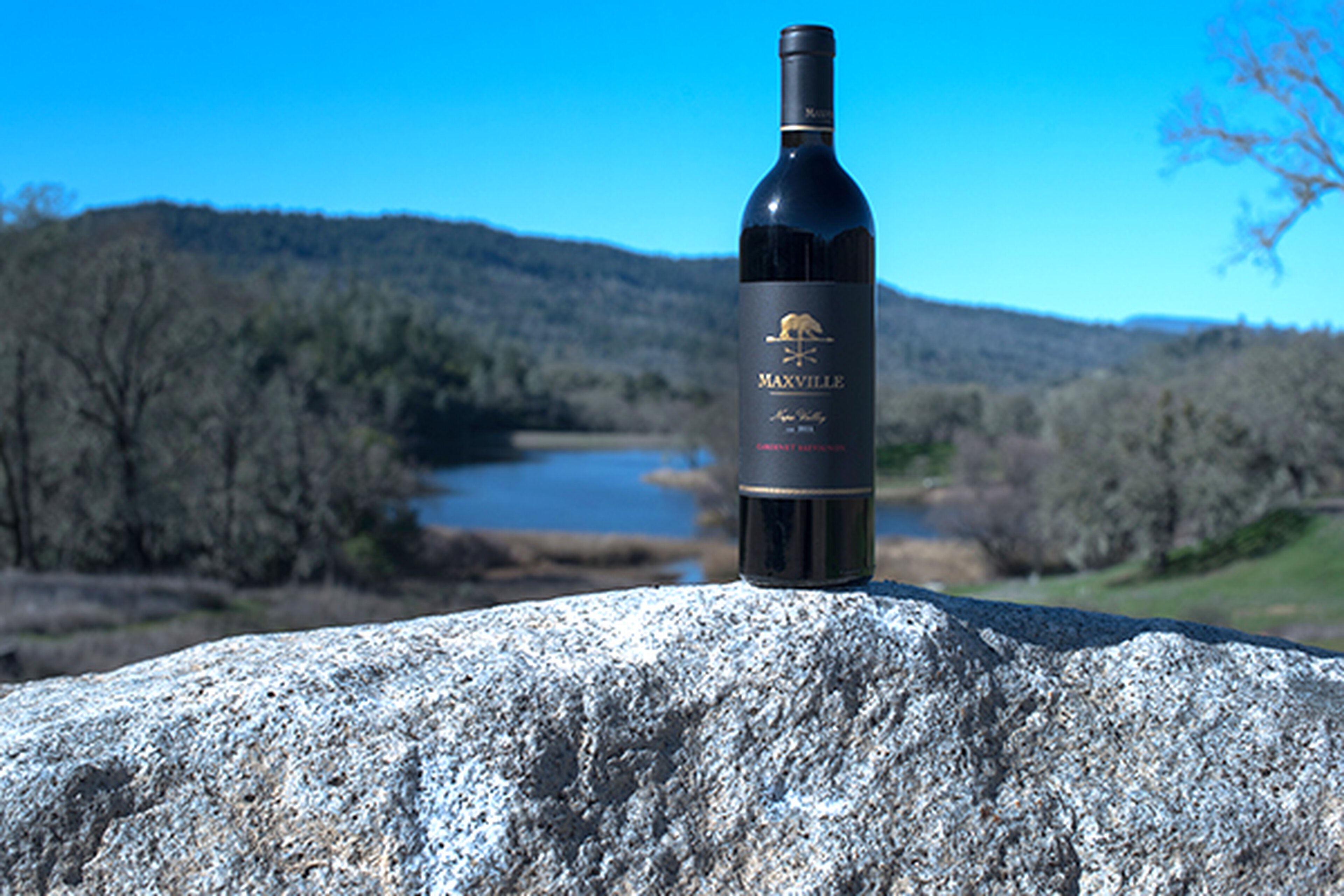 Maxville Winery wine bottle on a rock with scenic landscape background.