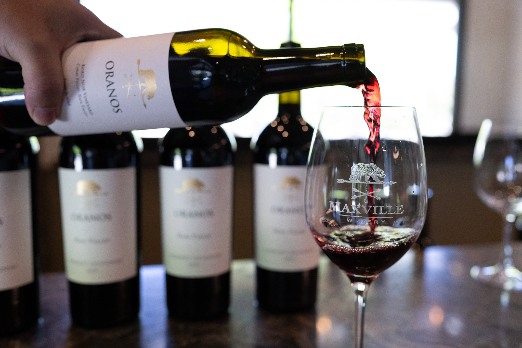 Pouring red wine into a glass at Maxville Winery, with bottles in the background.