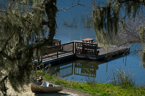 Scenic view of Maxville Winery with a wooden dock and boat on a calm lake surrounded by trees.